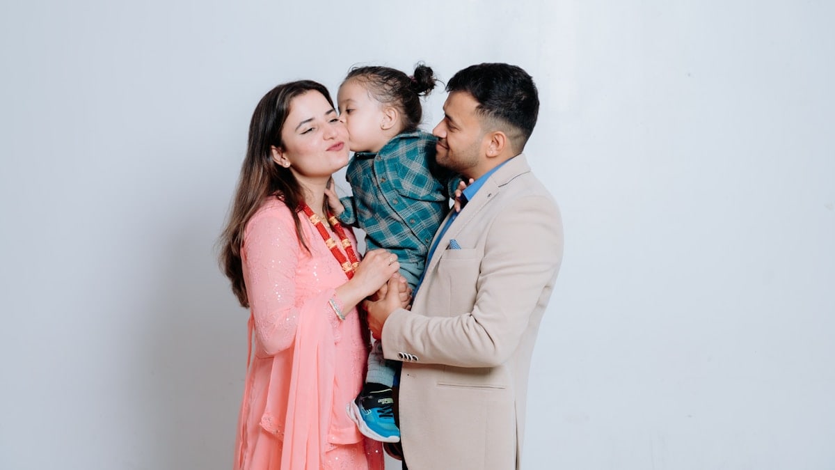 A man and a woman holding a baby in front of a white wall